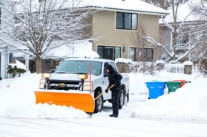 snowy Denver street with homes and a snow removal truck clearing the road assigned by hoa management company